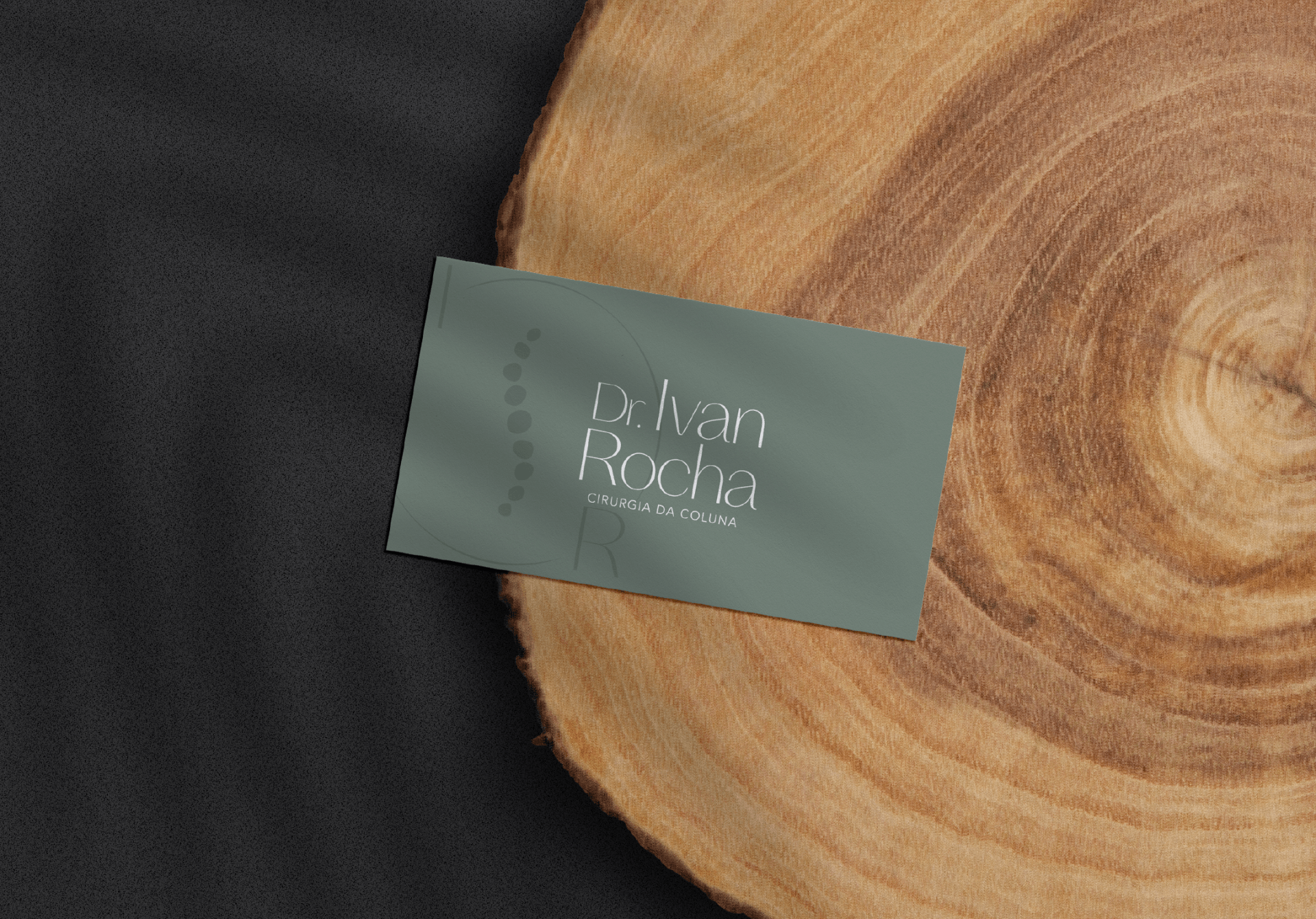Cartão de visitas verde contendo o logo do Dr. Ivan Rocha em cima de um suporte de madeira.