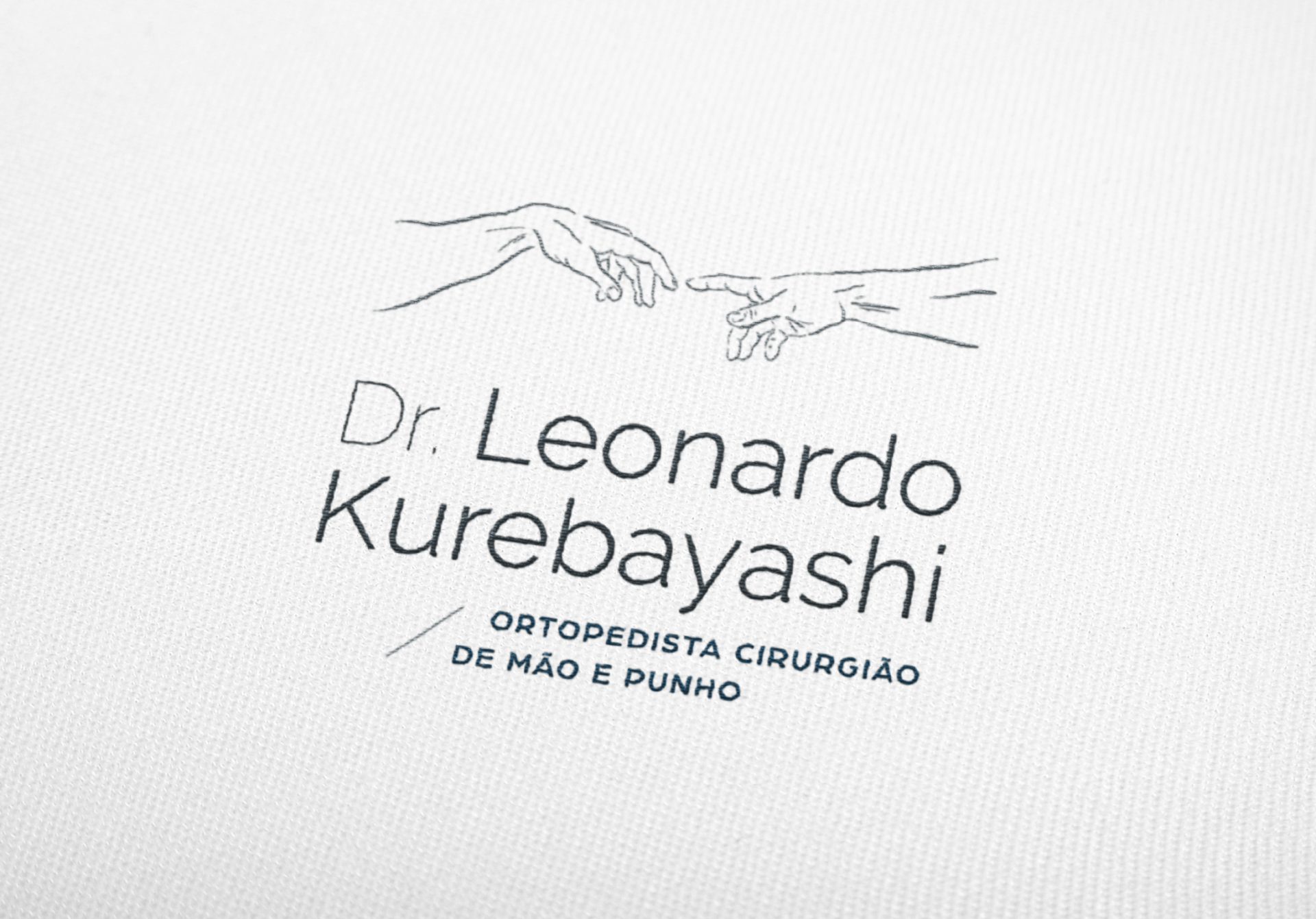 Logotipo do Dr. Leonardo Kurebayashi aplicado em tecido de jaleco médico, em alto relevo.