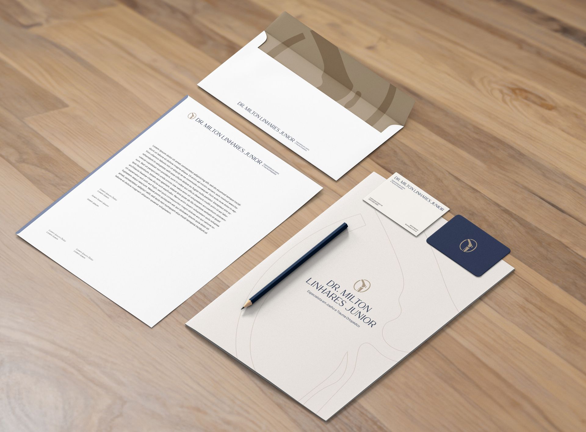 Conjunto de papelaria: papel timbrado, envelope, cartão de visita sobre superfície de madeira, cores claras e caneta.
