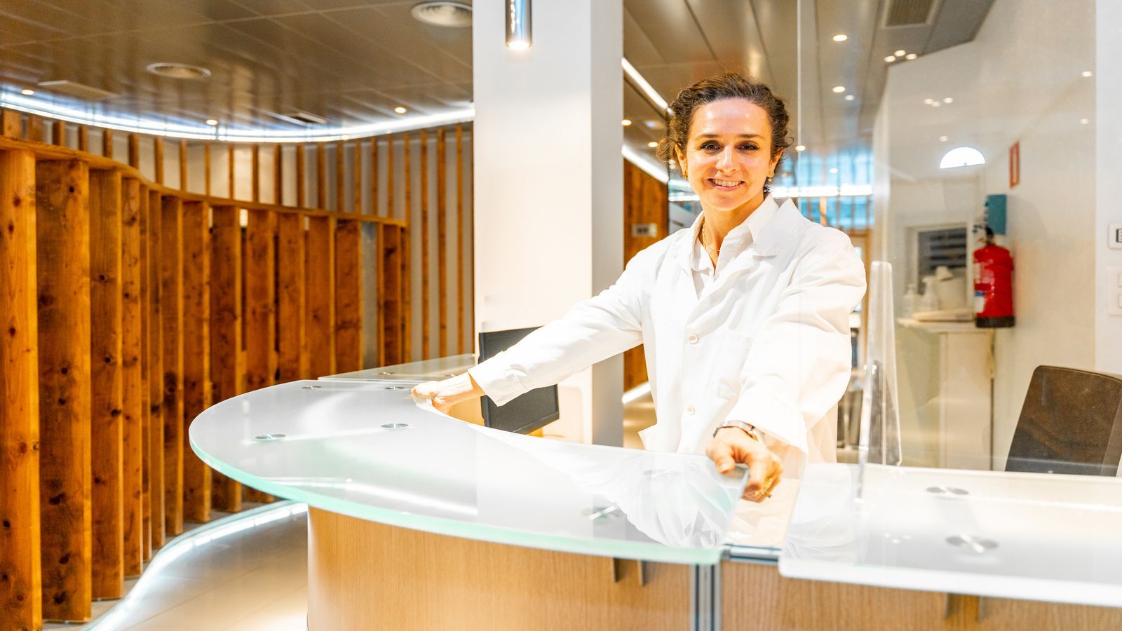 Recepcionista de clínica sorrindo ao receber os pacientes.