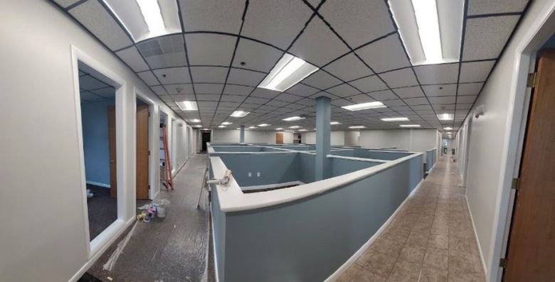 A long hallway with cubicles and a ceiling that is being painted.