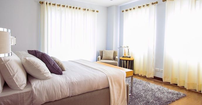 A bedroom with a bed , chair , rug and curtains.