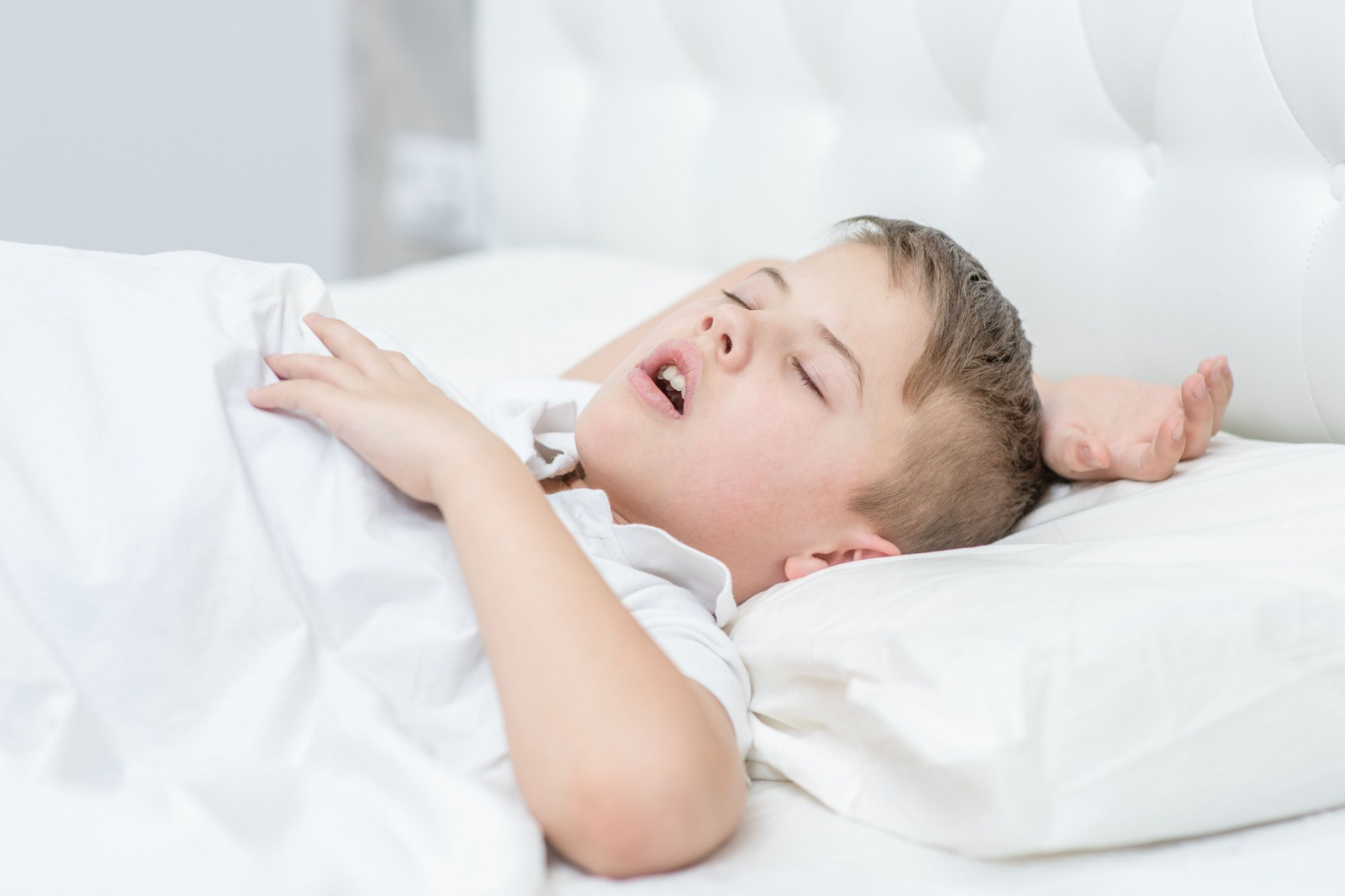 Un bambino dorme su un letto con la bocca aperta.