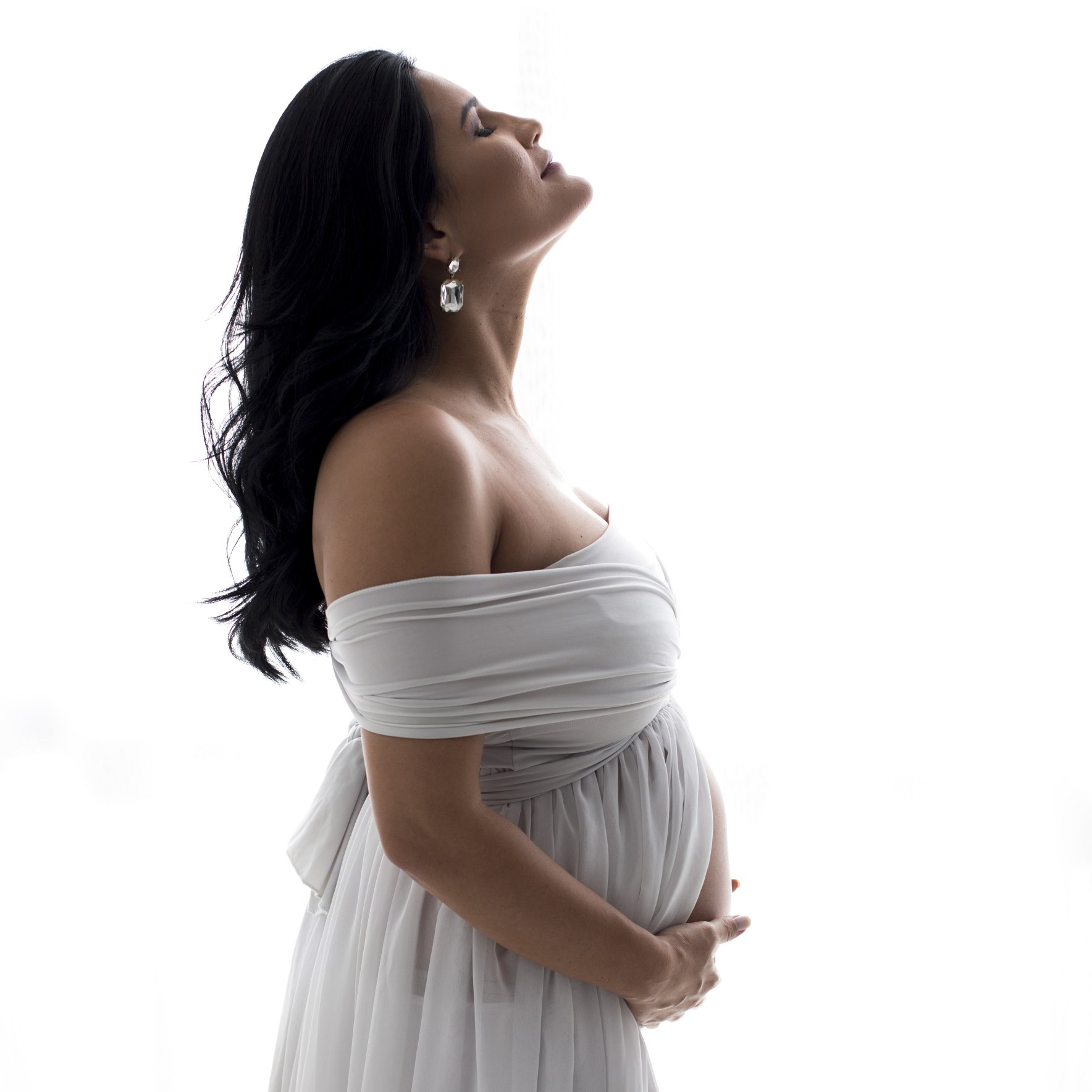 Una donna incinta vestita di bianco si tiene la pancia e guarda in alto.
