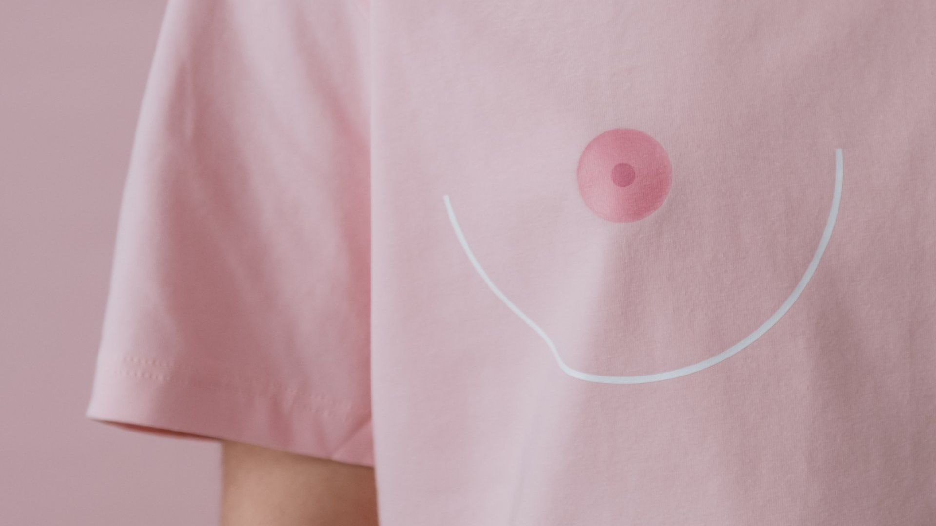 A woman is wearing a pink t-shirt with a pink breast embroidered on it.