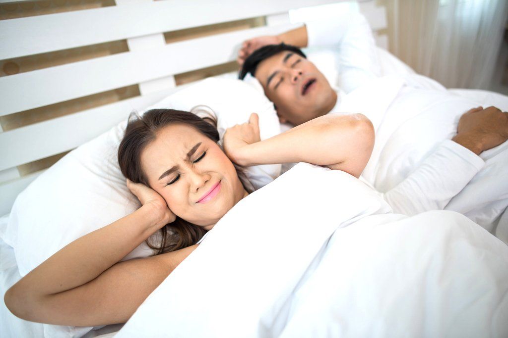 Una donna si copre le orecchie mentre un uomo russa a letto.