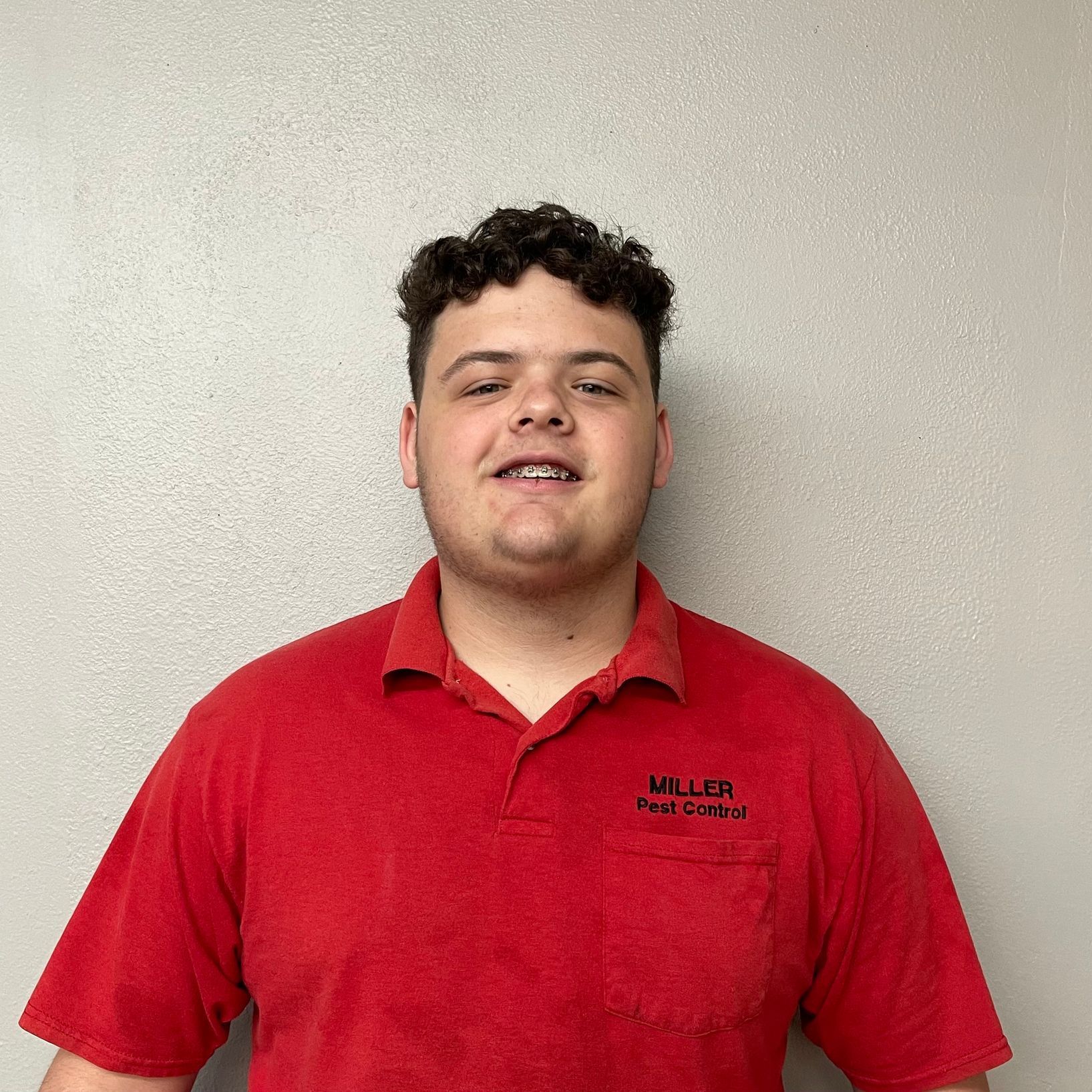 A young man wearing a red miller shirt is smiling for the camera