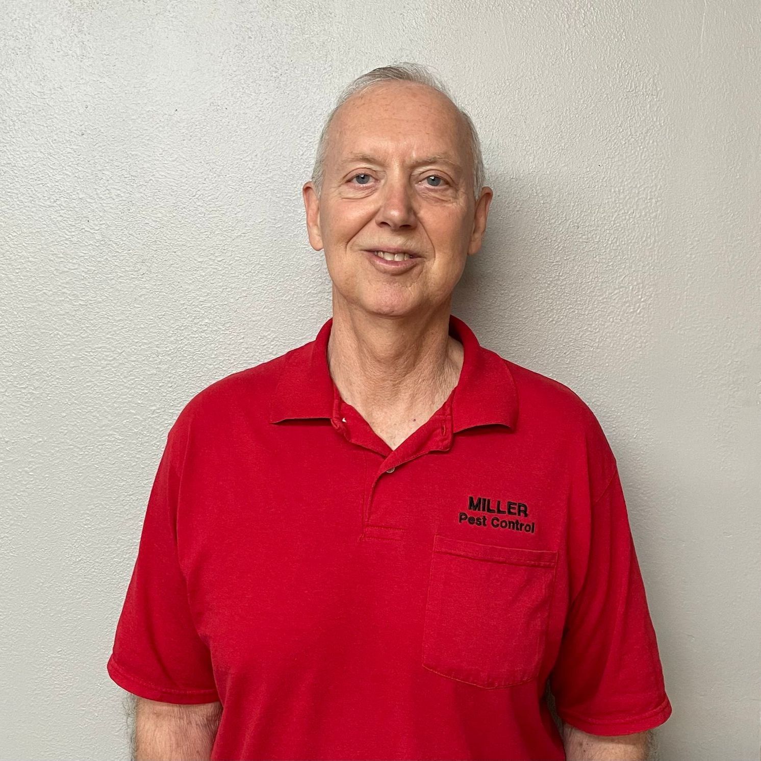 A man in a red shirt is standing in front of a white wall.