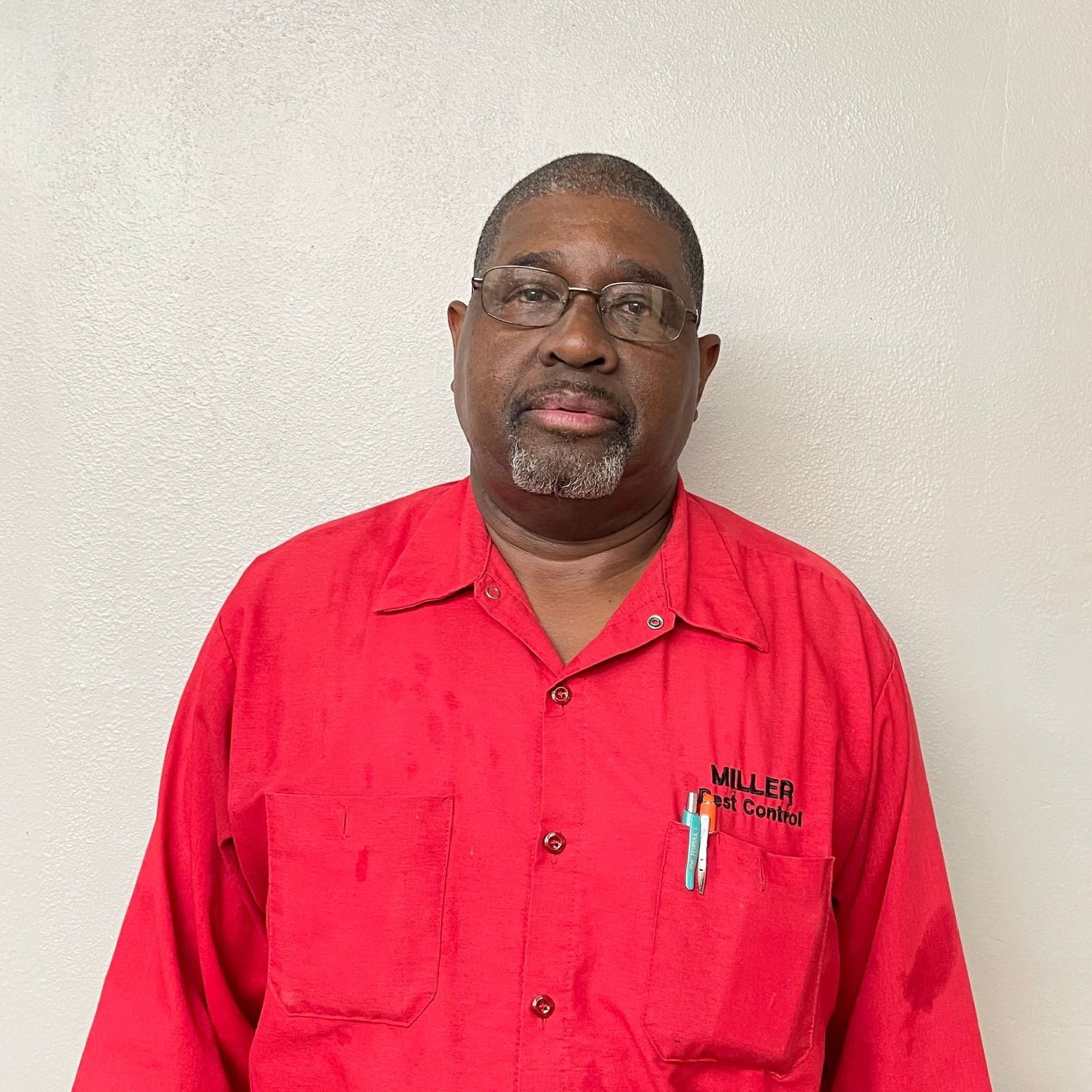 A man wearing glasses and a red shirt is standing in front of a white wall.