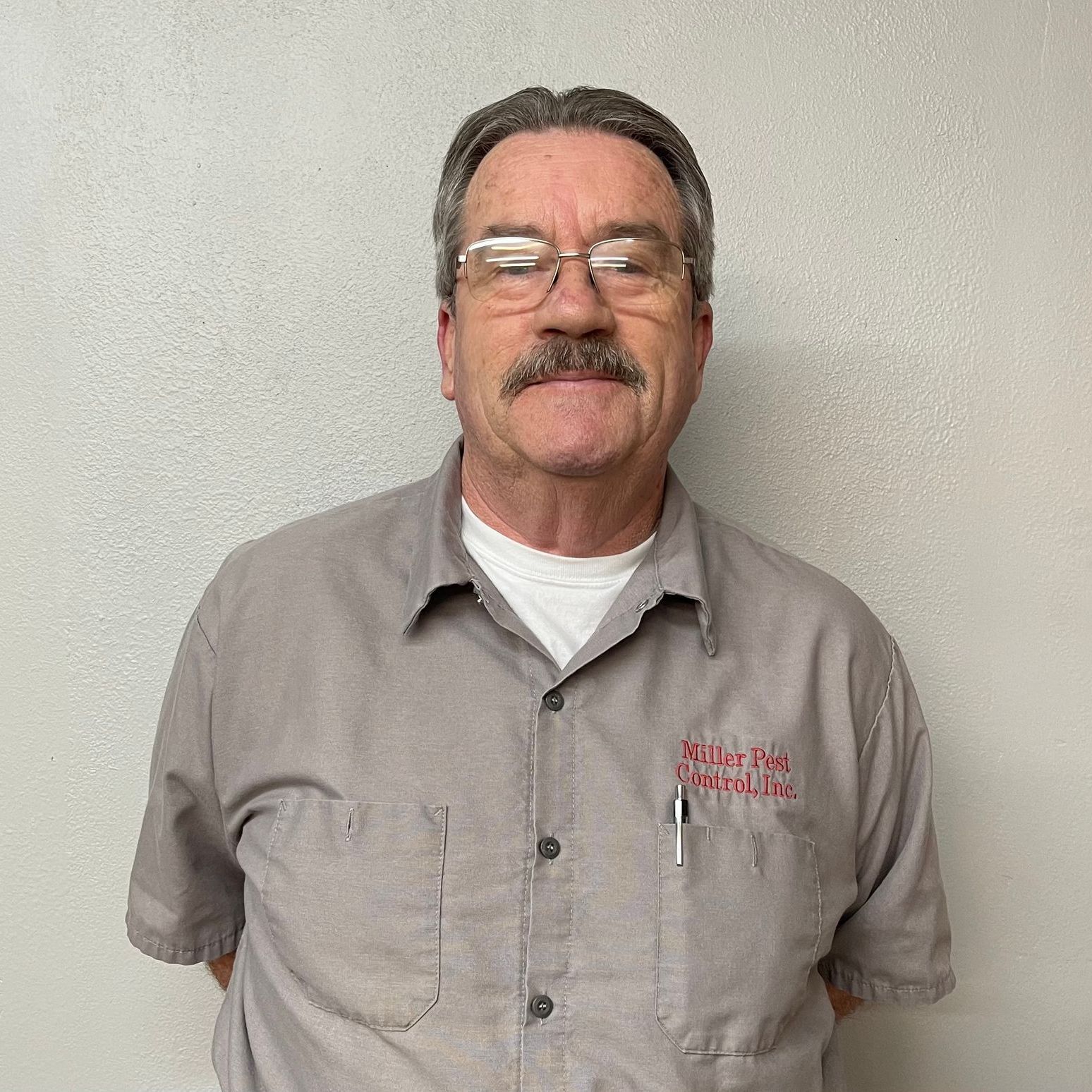 A man with a mustache and glasses is wearing a gray shirt.