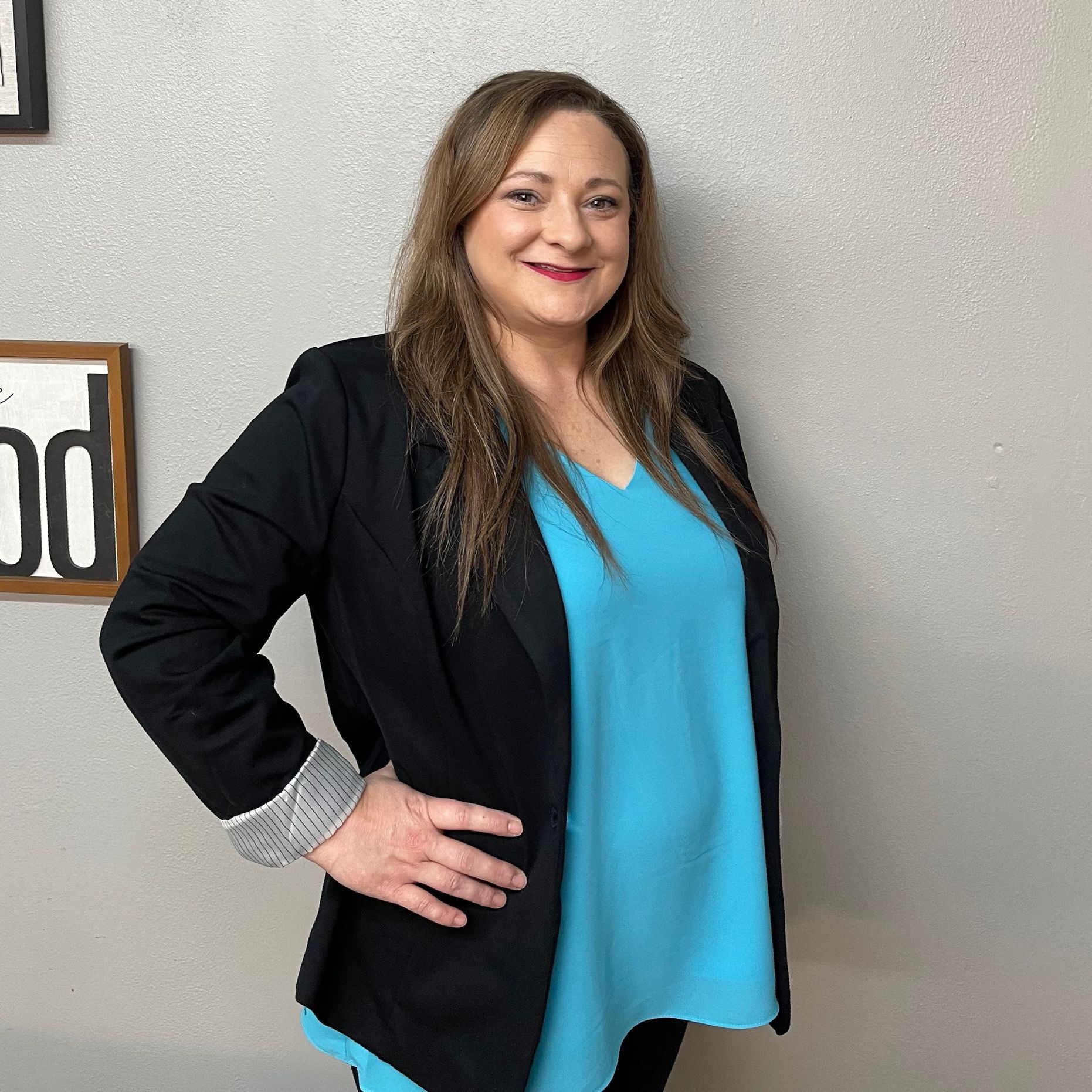 A woman wearing a black jacket and a blue shirt is standing with her hands on her hips.