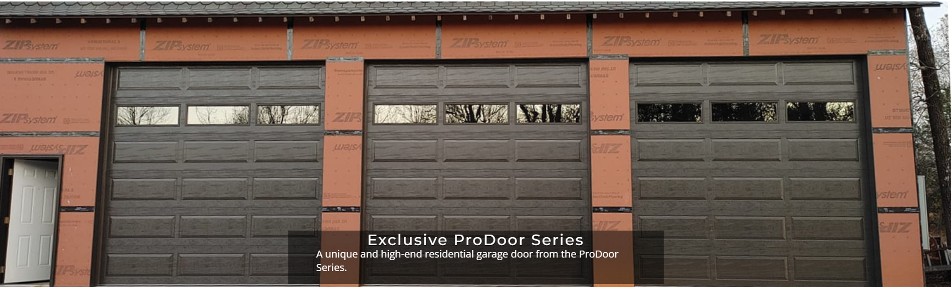 Three dark garage doors with small windows on a red brick building
