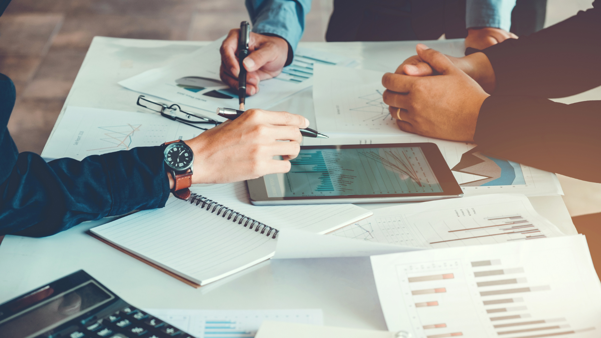 A group of people are sitting around a table looking at a tablet.