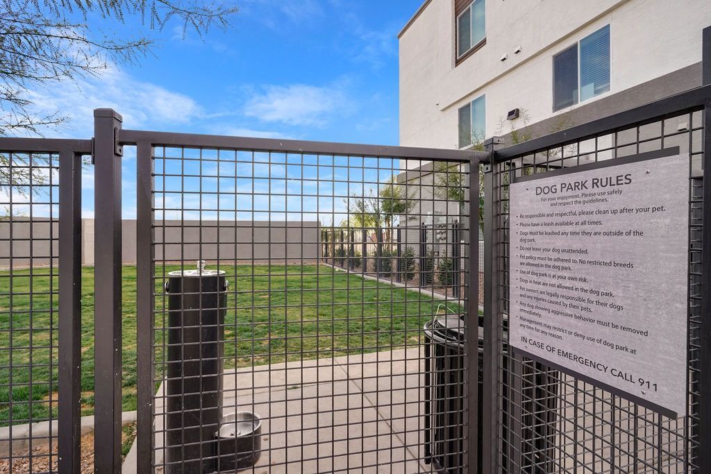 Gated dog park entrance with a large 'Dog Park Rules' sign beside an apartment building.