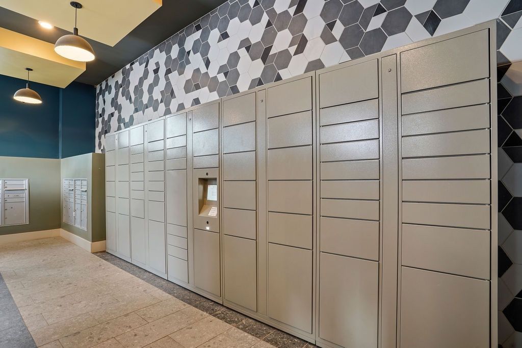 Row of gray parcel/mail lockers lining a tiled wall in a modern lobby.
