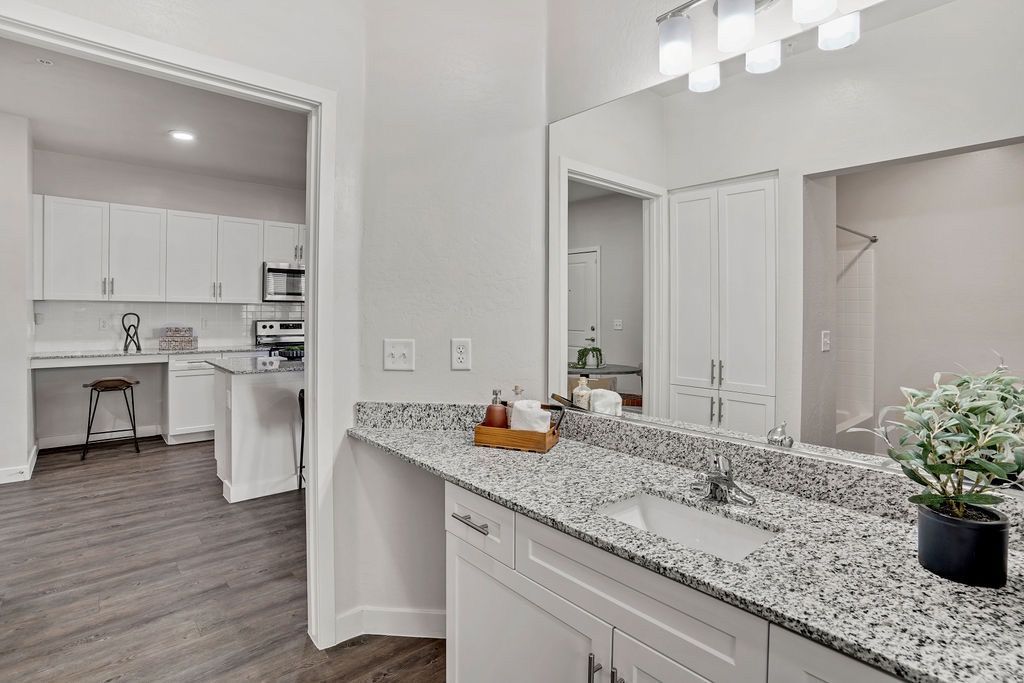 Bathroom vanity with granite countertop and sink; open kitchen visible in background.