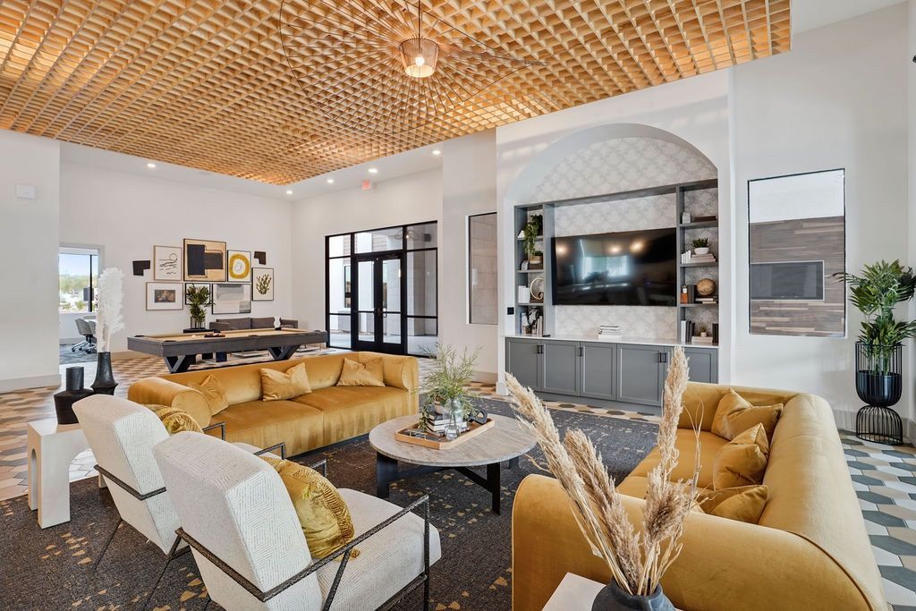 Modern resident lounge with mustard-yellow sofas, accent chairs, a coffee table, and a wall-mounted TV.