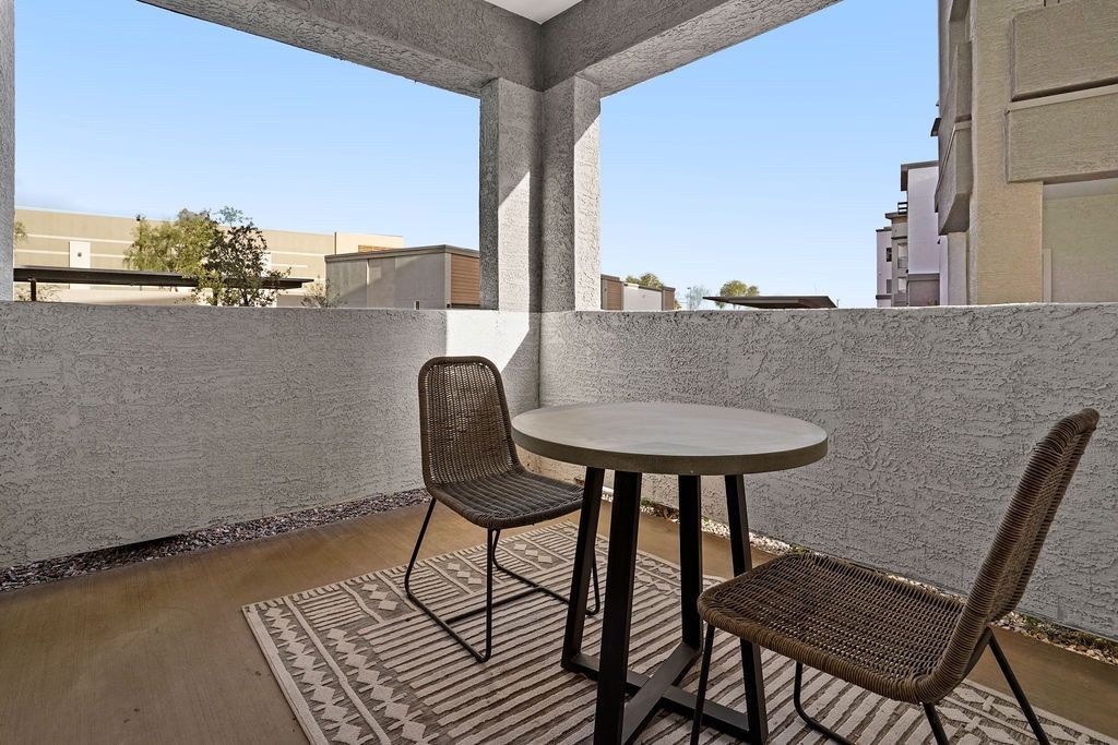 Outdoor apartment balcony with a round table and two wicker chairs against concrete walls.