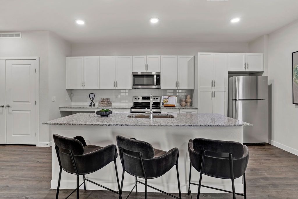 Modern kitchen with white cabinets, granite island, and stainless-steel appliances.