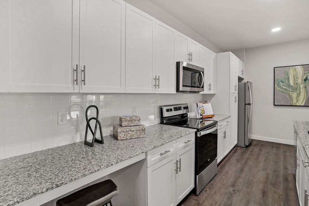 Modern white kitchen with granite countertops, stainless steel appliances, and wood-look flooring.