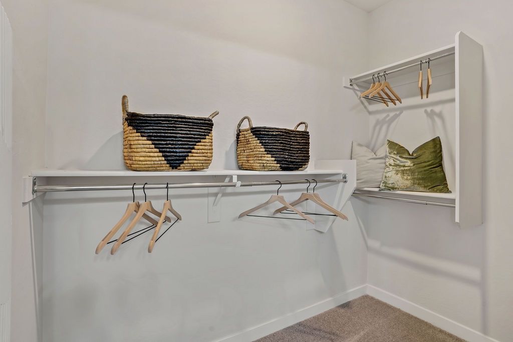 White walk-in closet with shelves, a hanging rod, and woven baskets.
