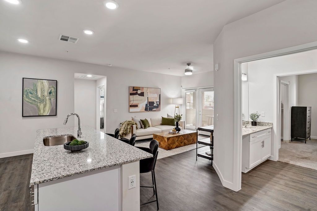 Open-concept kitchen with granite island and adjacent living room in a modern apartment.