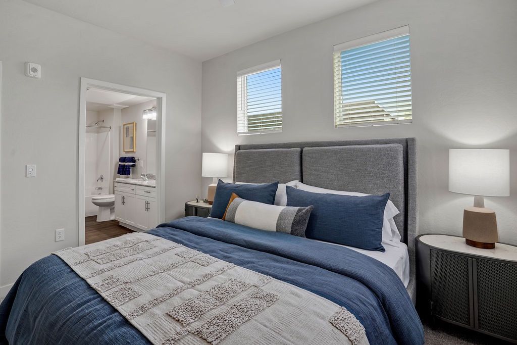 Bedroom with a gray upholstered bed, two nightstands, and an open doorway to a connected bathroom.