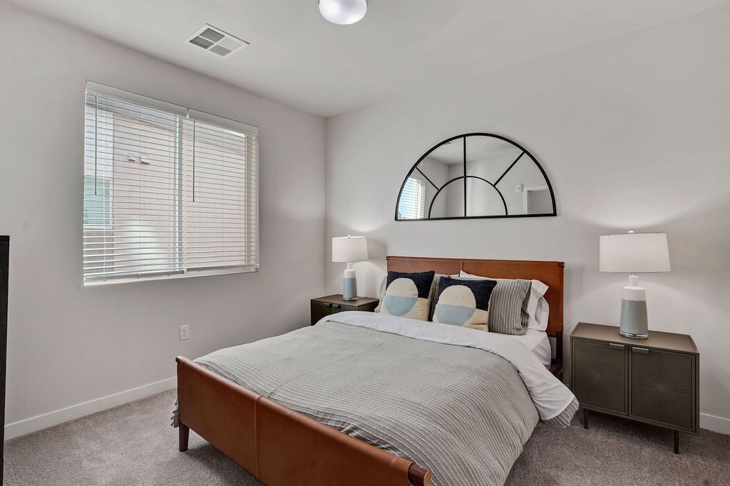 Bedroom in an apartment with a wooden bed, two nightstands, lamps, and a semicircular black-framed mirror.
