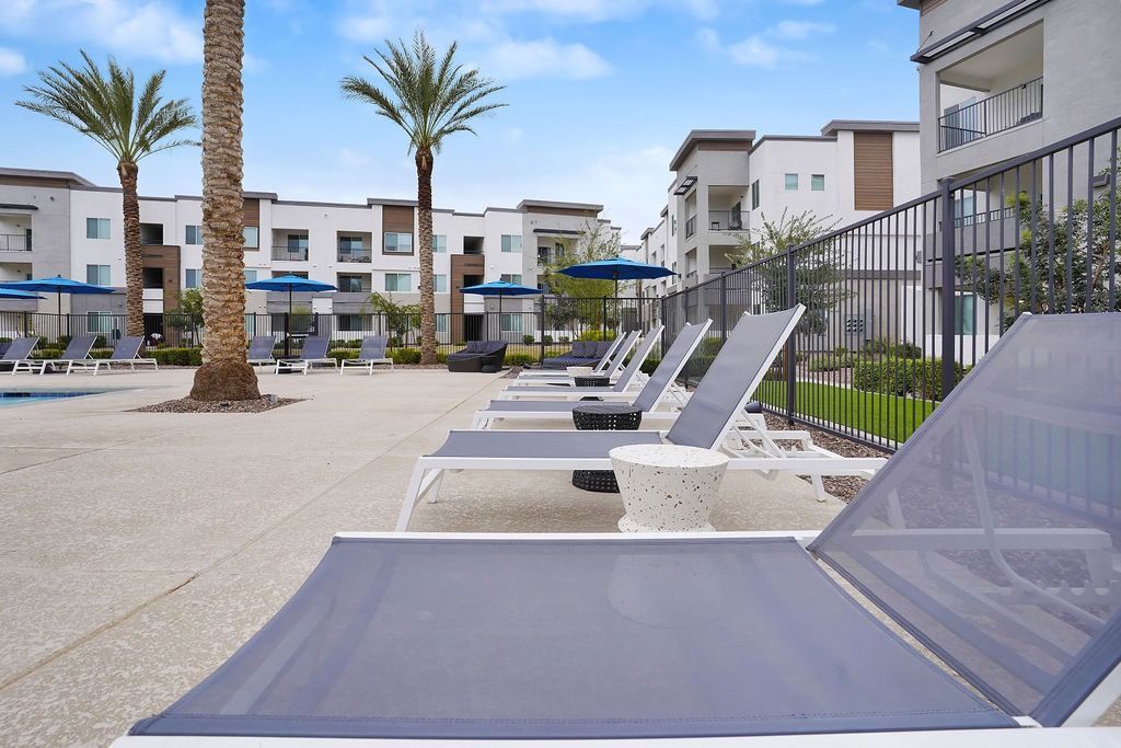Poolside lounge chairs and blue umbrellas at an apartment complex courtyard.