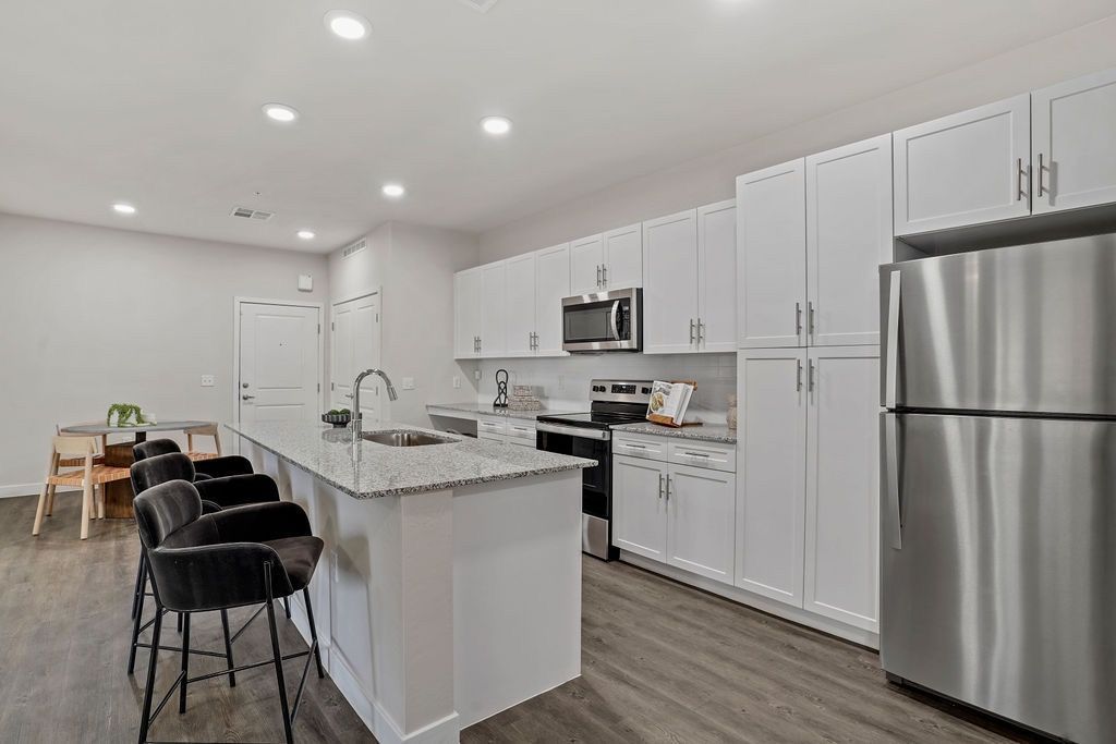 Modern apartment kitchen with white cabinets, stainless steel appliances, and an island with seating.
