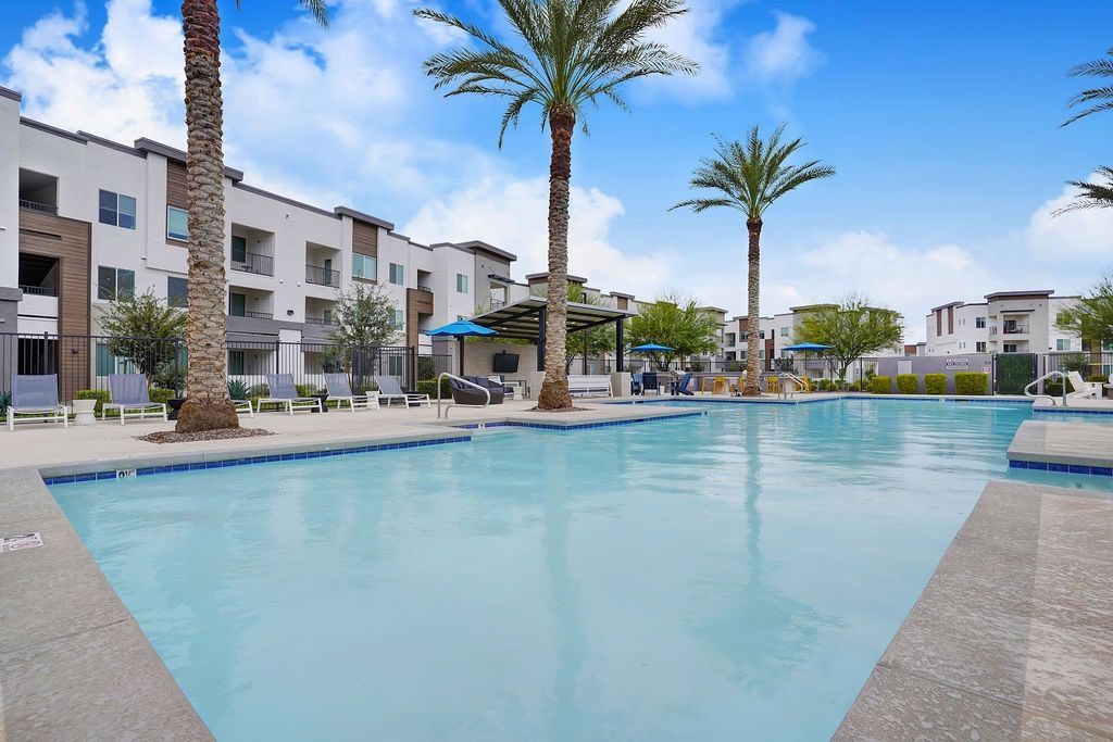 Outdoor apartment pool with palm trees, lounge chairs, and shaded seating.