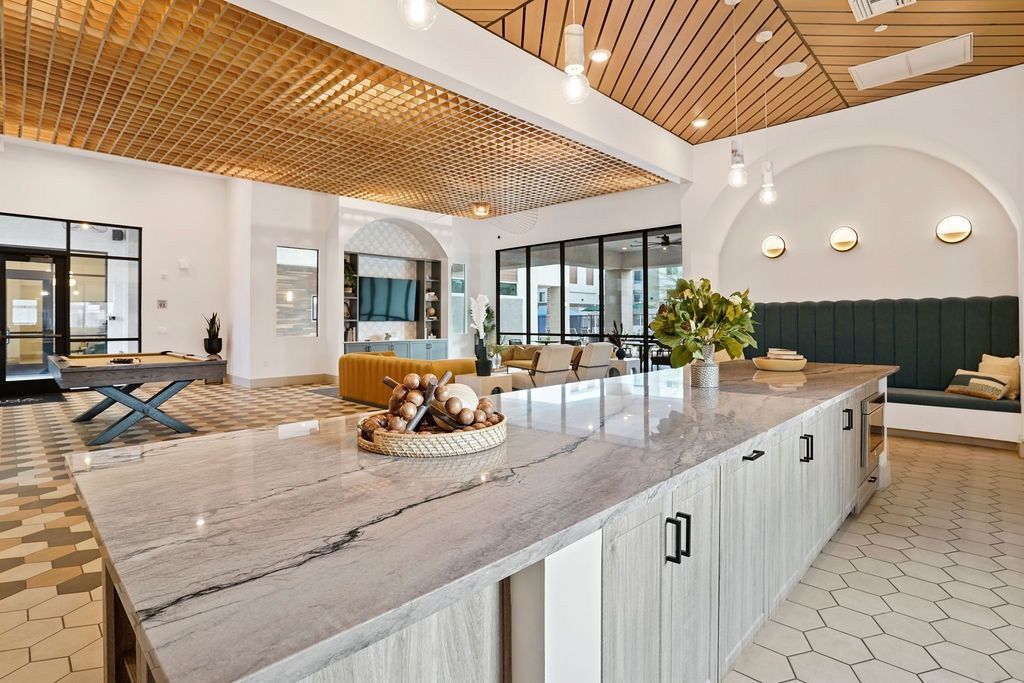 Open indoor community lounge with a marble island, modern seating, wood ceiling, and hex tile flooring.
