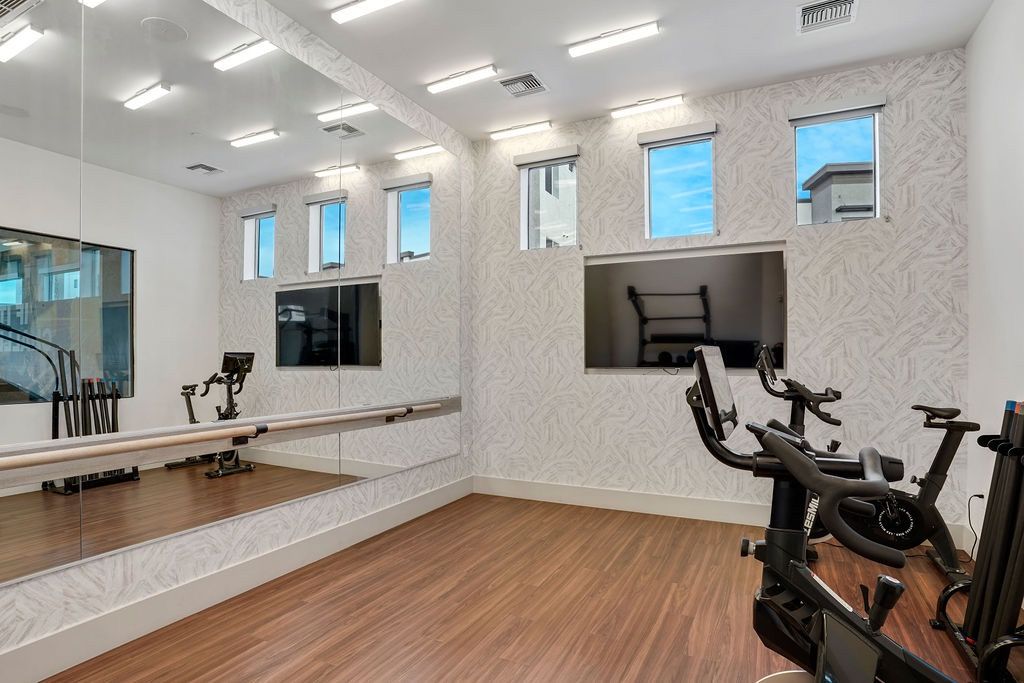 Indoor community gym with stationary bikes, a mirrored wall, and wood-like flooring.