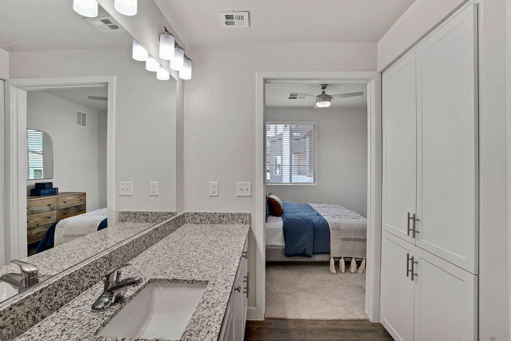 Bathroom vanity with granite countertop, double sink, and doorway to a bedroom with a window.