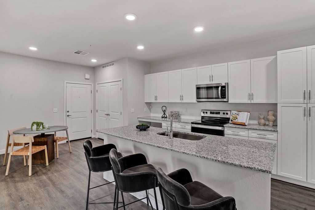 Open kitchen with island, granite countertops, white cabinets, and stainless-steel appliances.