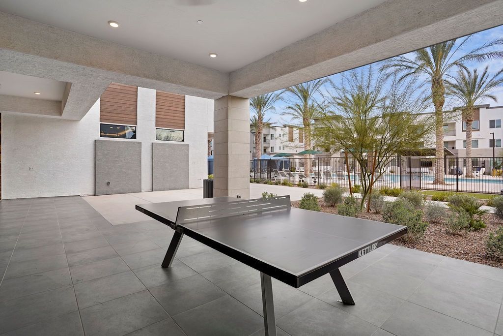 Covered outdoor amenity area with a ping-pong table; pool and palm trees visible in the background.