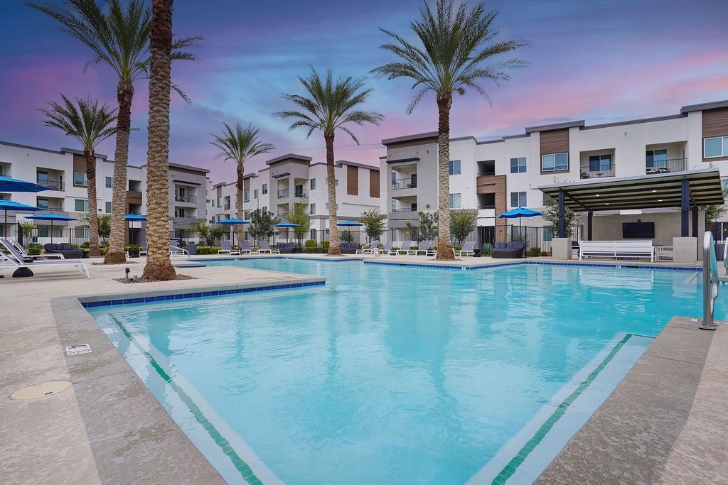 Outdoor apartment community pool with palm trees, lounge chairs, and a shaded seating area.