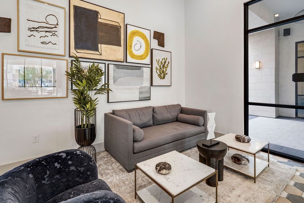 Modern community lounge with gray sofa, plant, and large glass entry door.