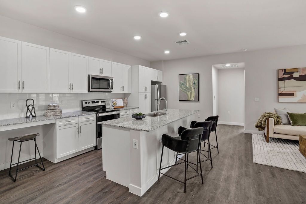 Modern white kitchen with granite island, stainless appliances, and open living area.