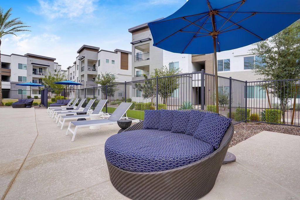 Outdoor community pool area with lounge chairs and blue umbrellas in a modern apartment complex.