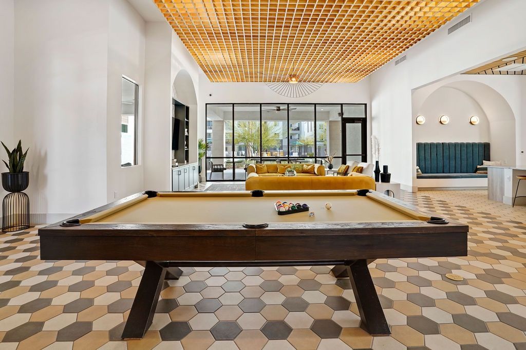 Modern community lounge with a pool table, hexagonal tile floor, and seating.