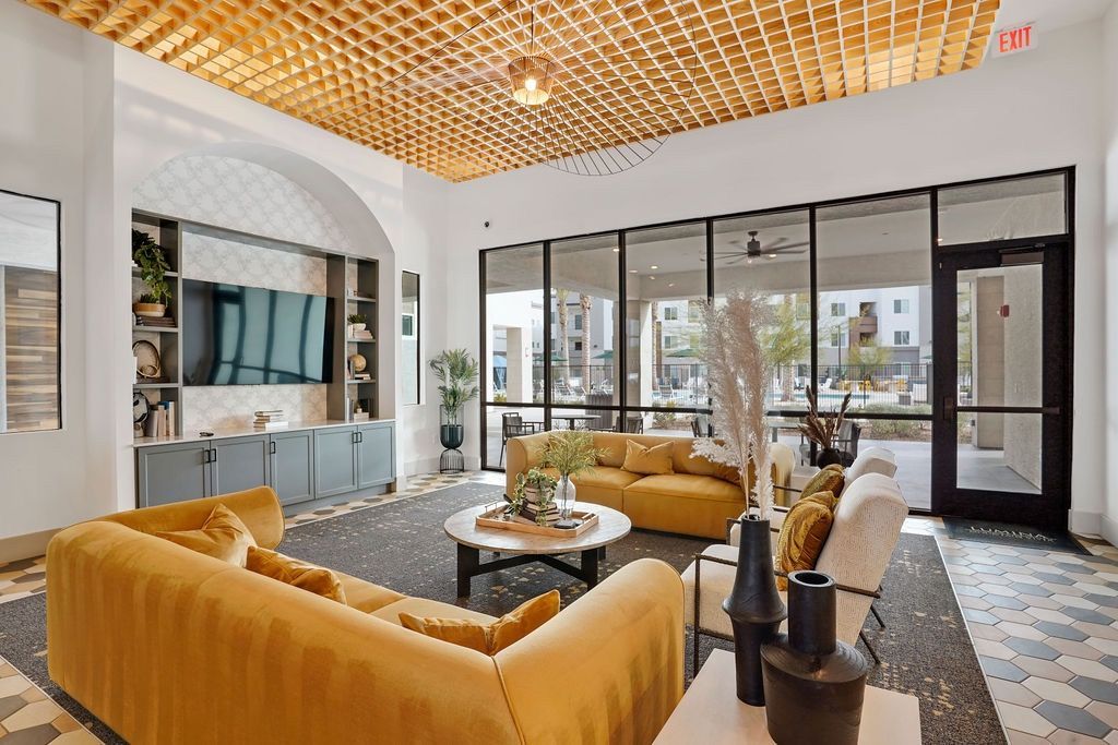 Interior community lounge with mustard-yellow sofas, a round coffee table, and large glass doors.