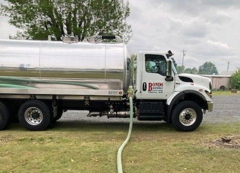 A tanker truck is parked in a grassy field with a hose attached to it.