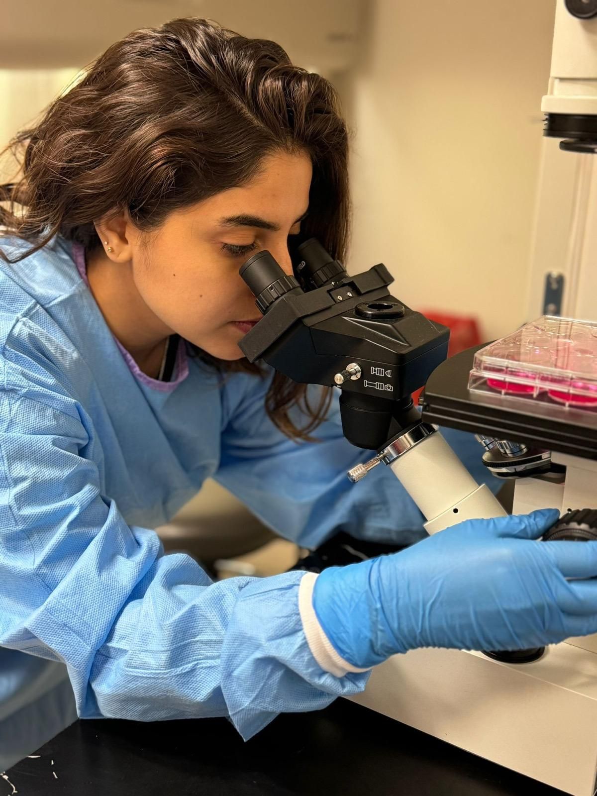 A woman is looking through a microscope in a lab.