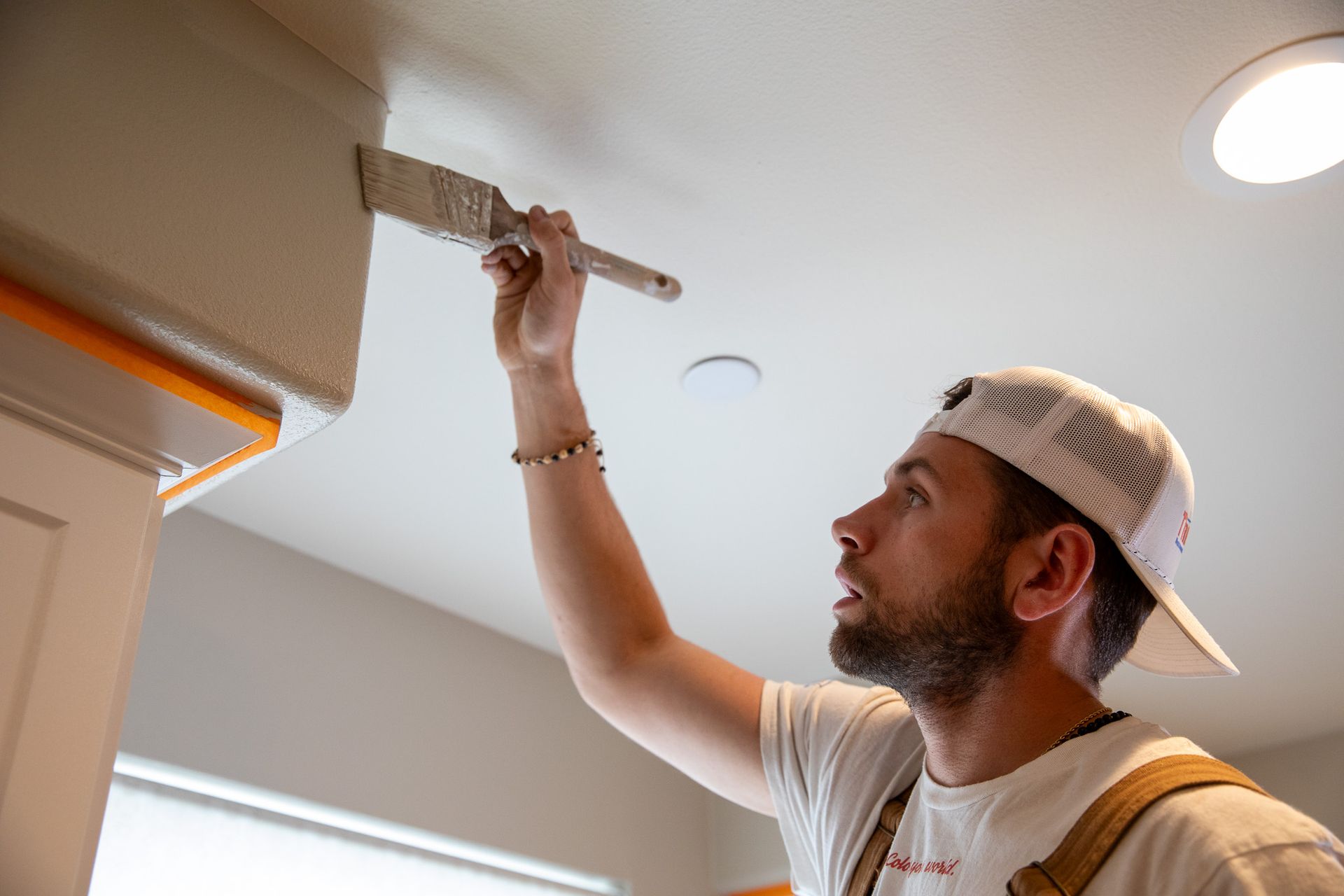 A man is painting the ceiling of a room with a brush.