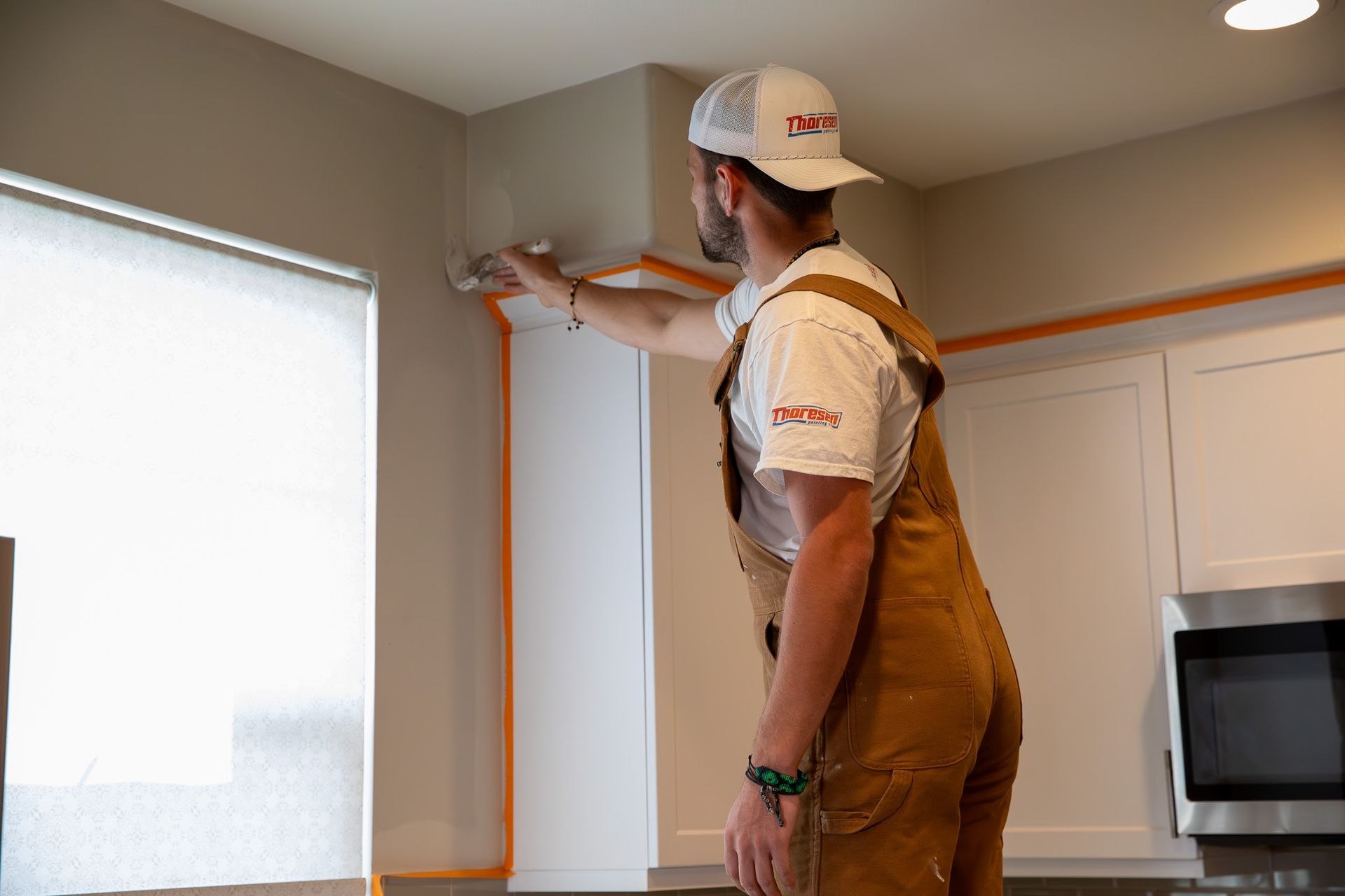 A man is painting a wall in a kitchen.