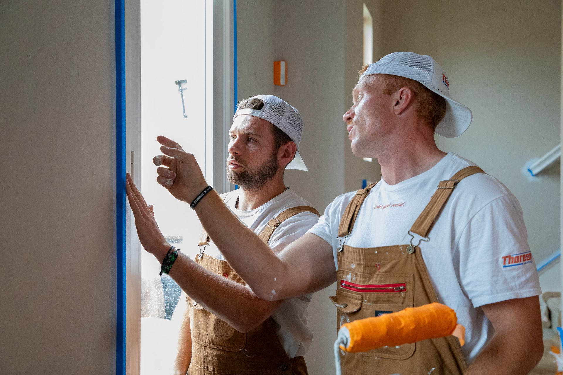 Two men are standing next to each other in a room looking at a wall.