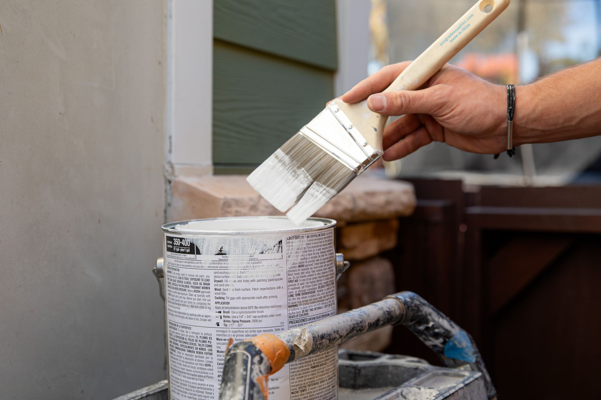 A person is holding a brush over a can of paint.