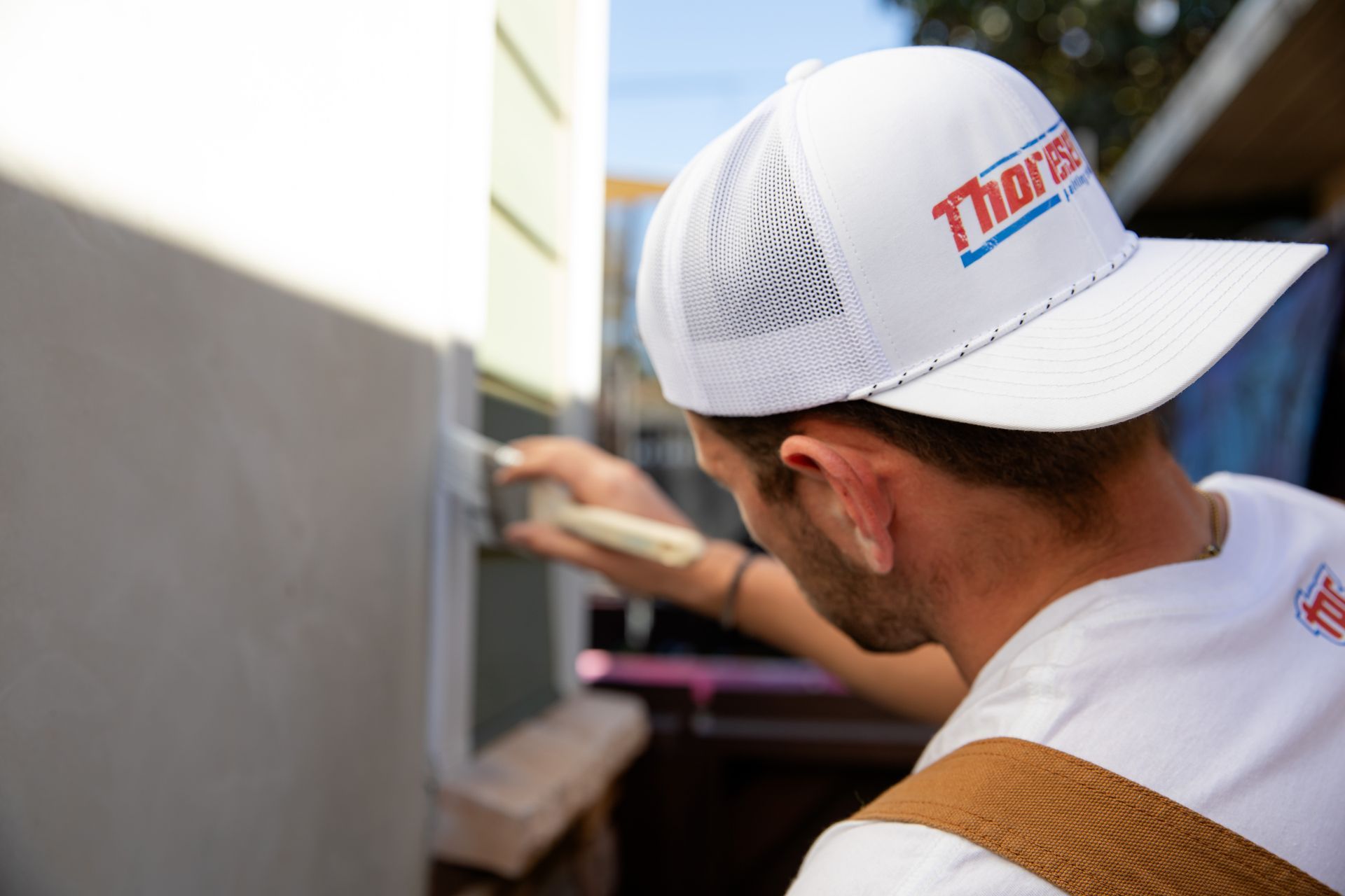 A man wearing a white hat is painting a wall with a brush.