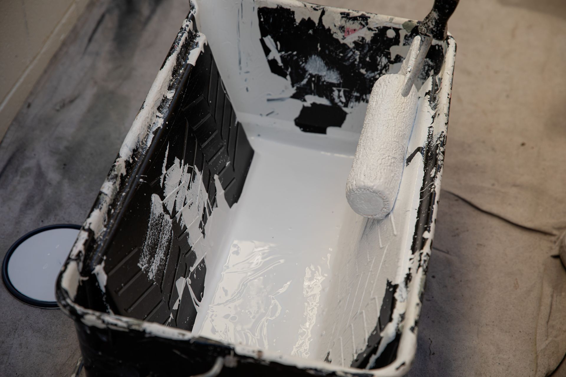 A bucket filled with white paint and a paint roller.